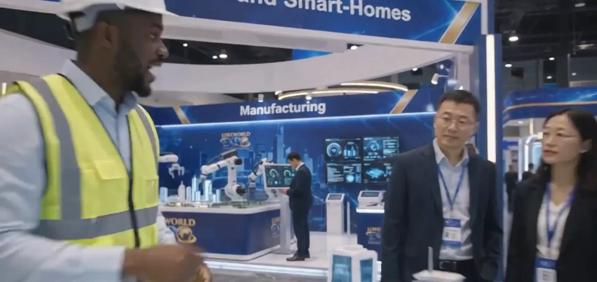 An engineer in a safety vest talking with two visitors at the manufacturing stand